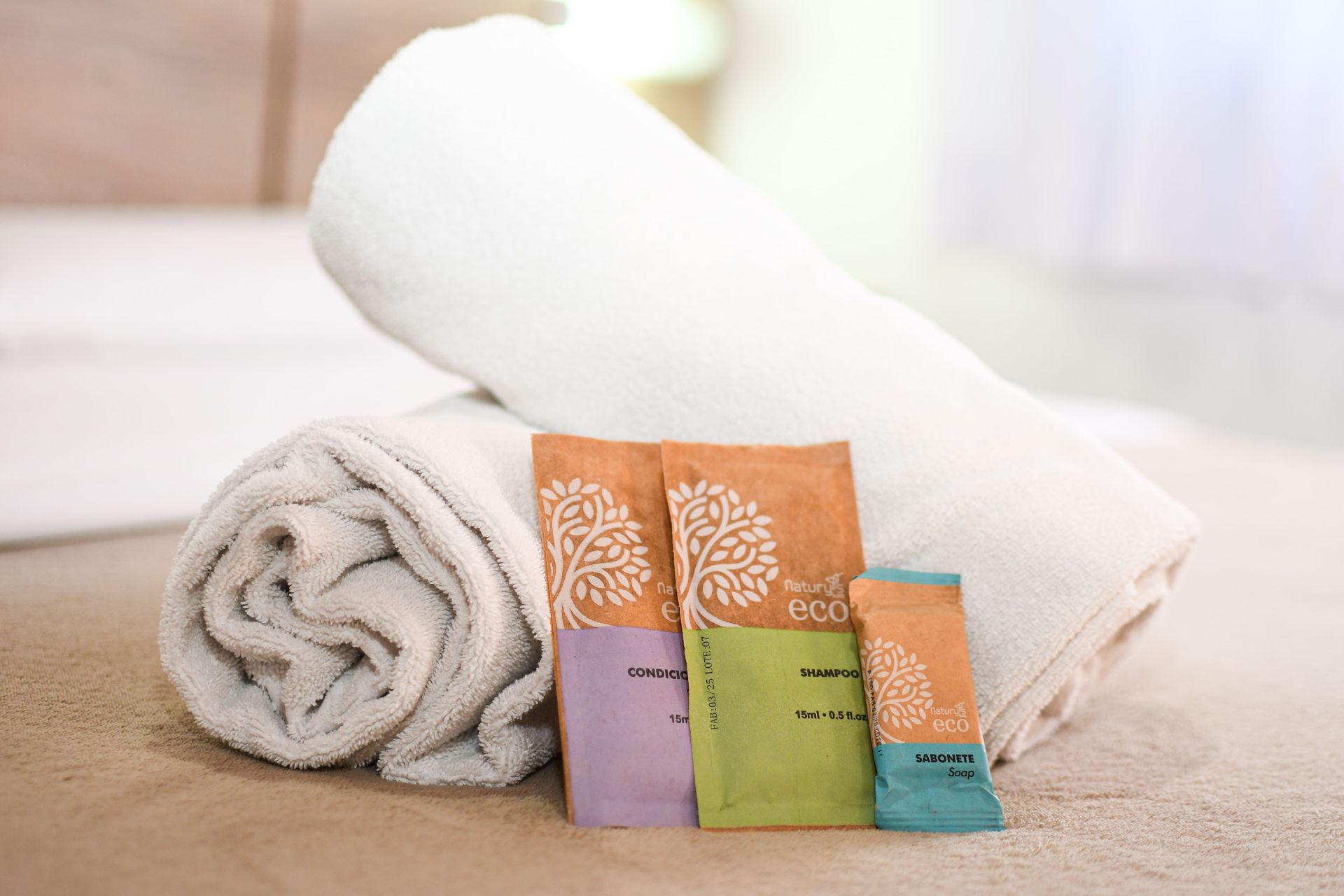 Uma toalha enrolada em cima da cama ao lado de uma bolsa de produtos de higiene.