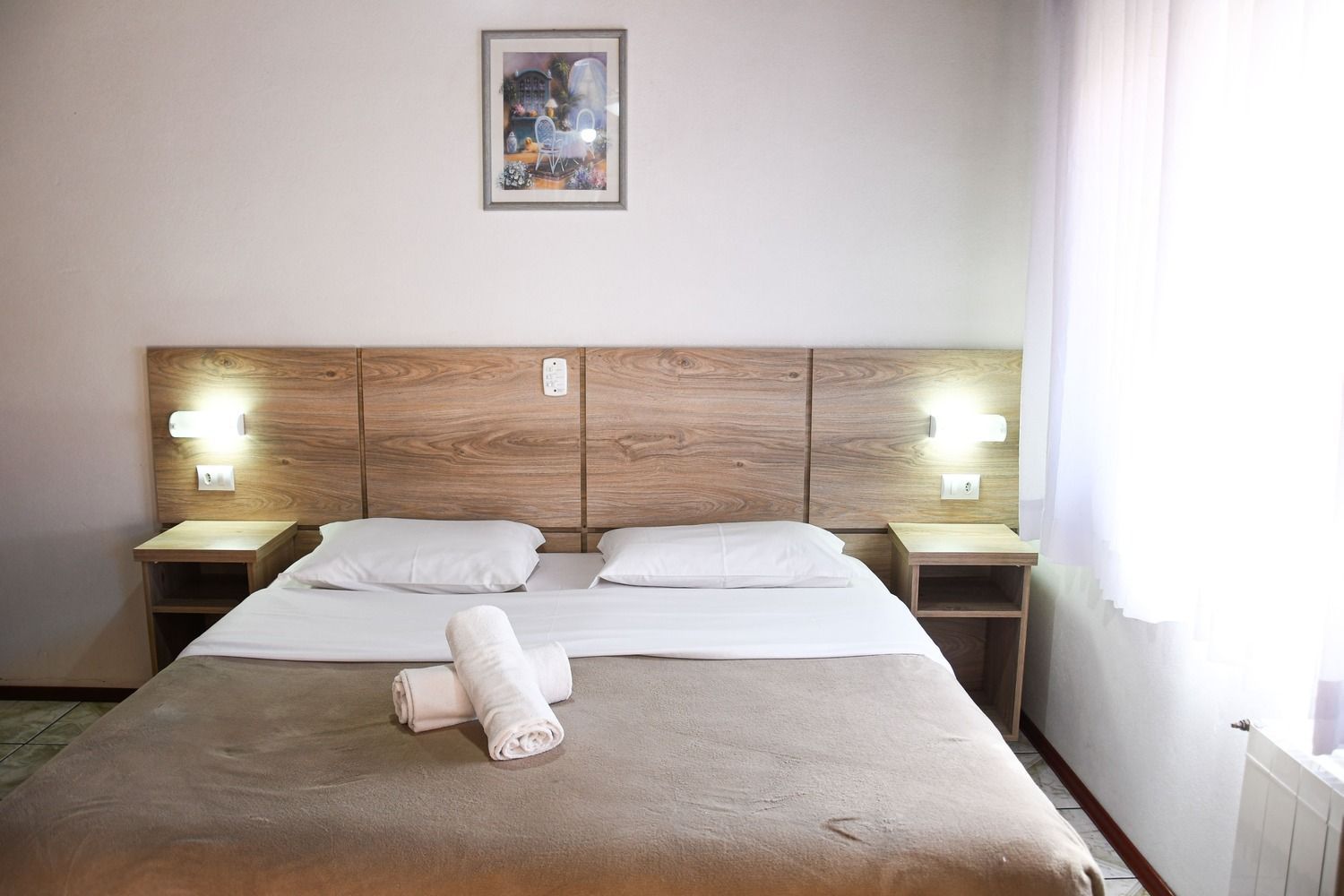 Um quarto de hotel com uma cama, mesas de cabeceira e um quadro na parede.