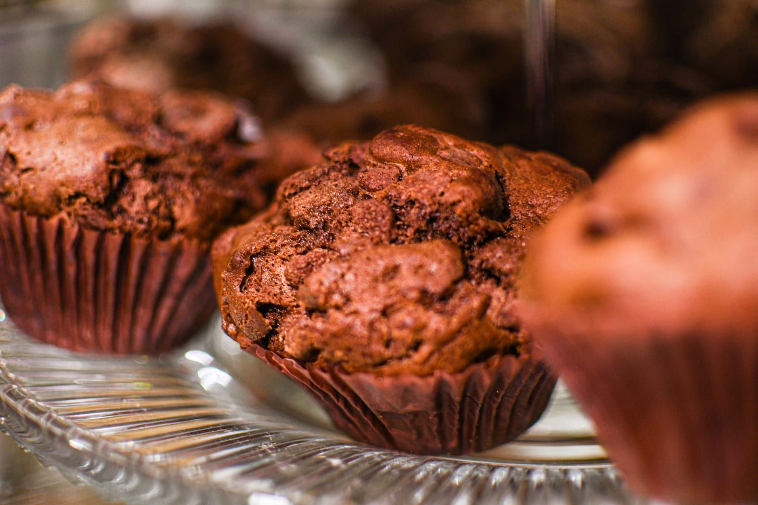 Um close de três muffins de chocolate em um prato de vidro.