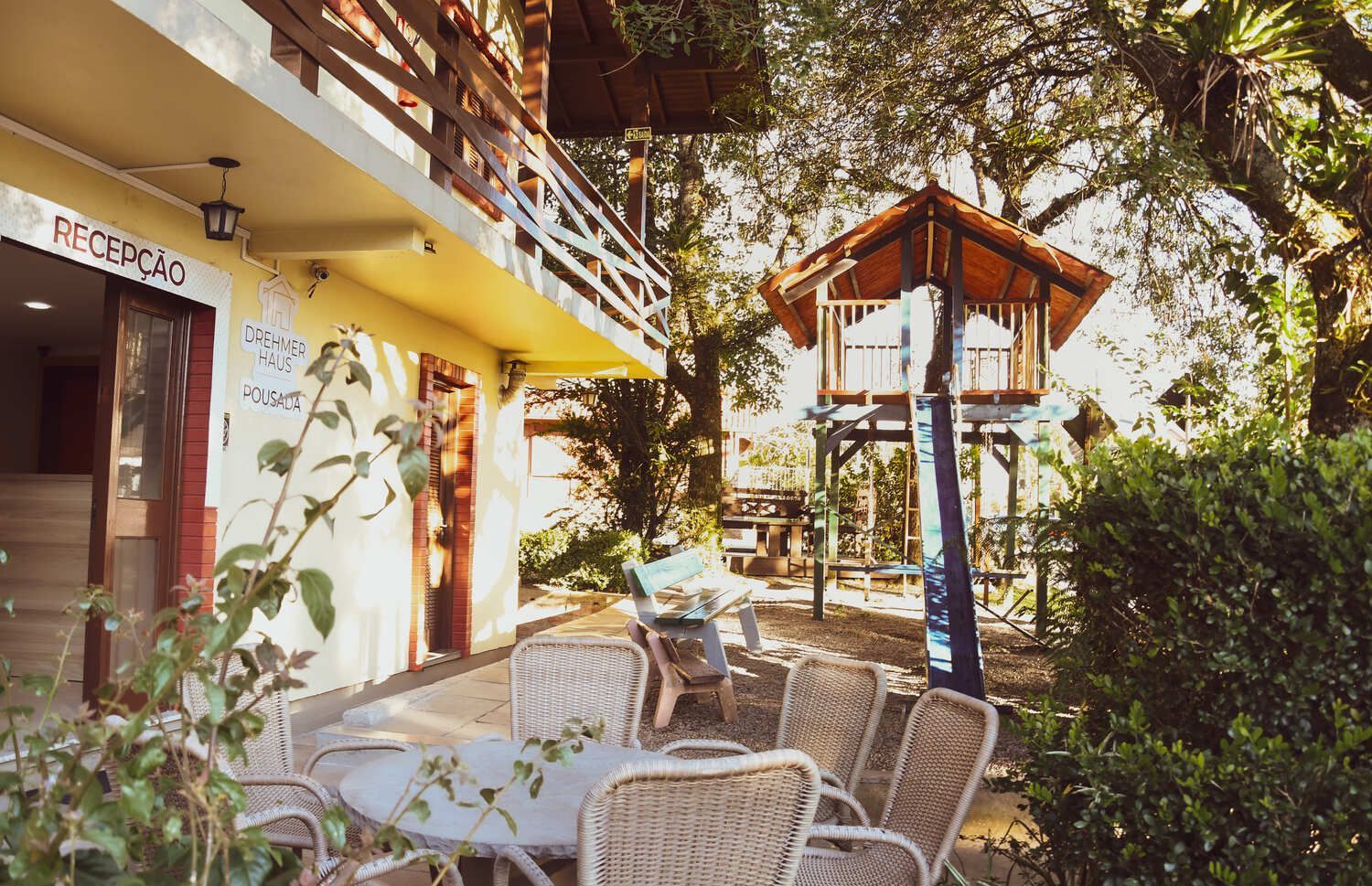 Um pátio com mesas e cadeiras e uma casa na árvore ao fundo.