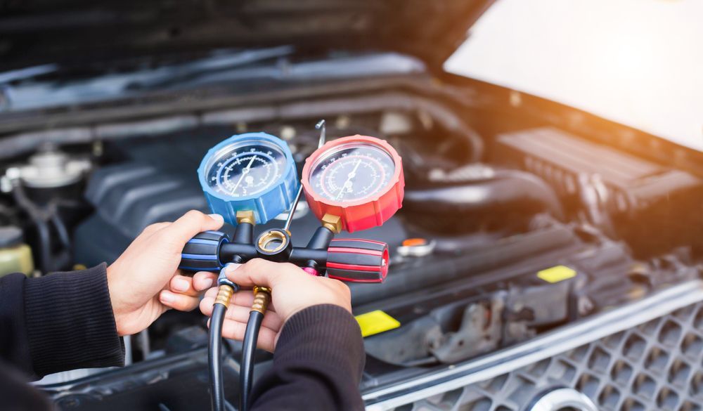 A Person Is Holding A Gauge In Front Of A Car Engine — North Coast Mobile Auto Air Conditioning In Darwin, NT