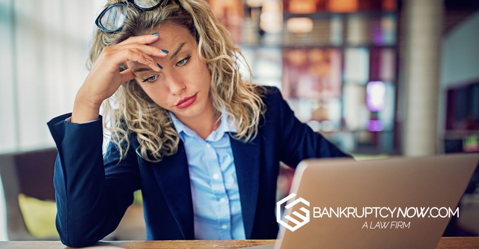Woman looking stressed at a laptop with hand on her forehead. Restaurant setting.
