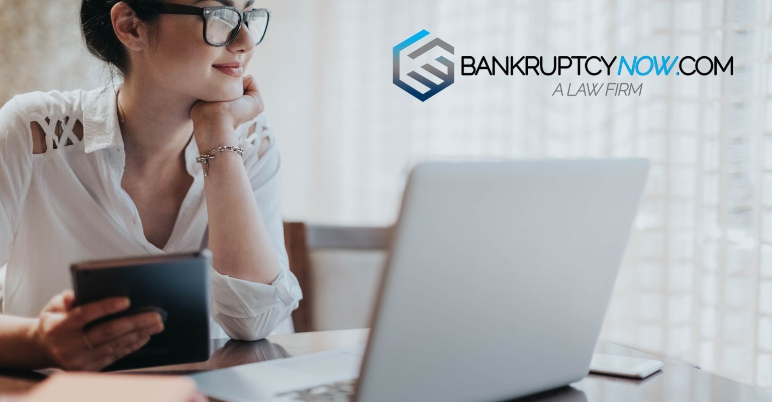 Woman with glasses uses a laptop and tablet, next to a 