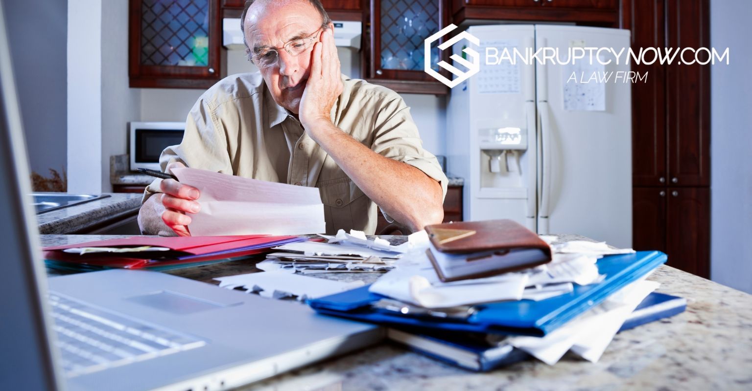 Man stressed at a kitchen counter, surrounded by bills and a laptop.