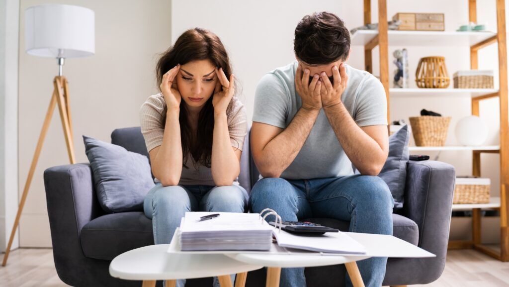 Couple sitting on couch, stressed and looking at bills.