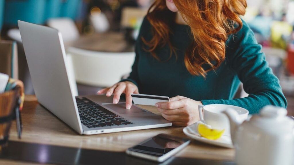 Woman with red hair using laptop, holding credit card. Cafe setting.