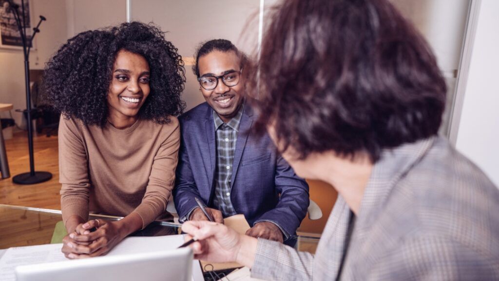 Couple smiles while reviewing documents with a professional in a bright office setting.