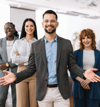 Smiling business team in office setting; man with open arms in front.