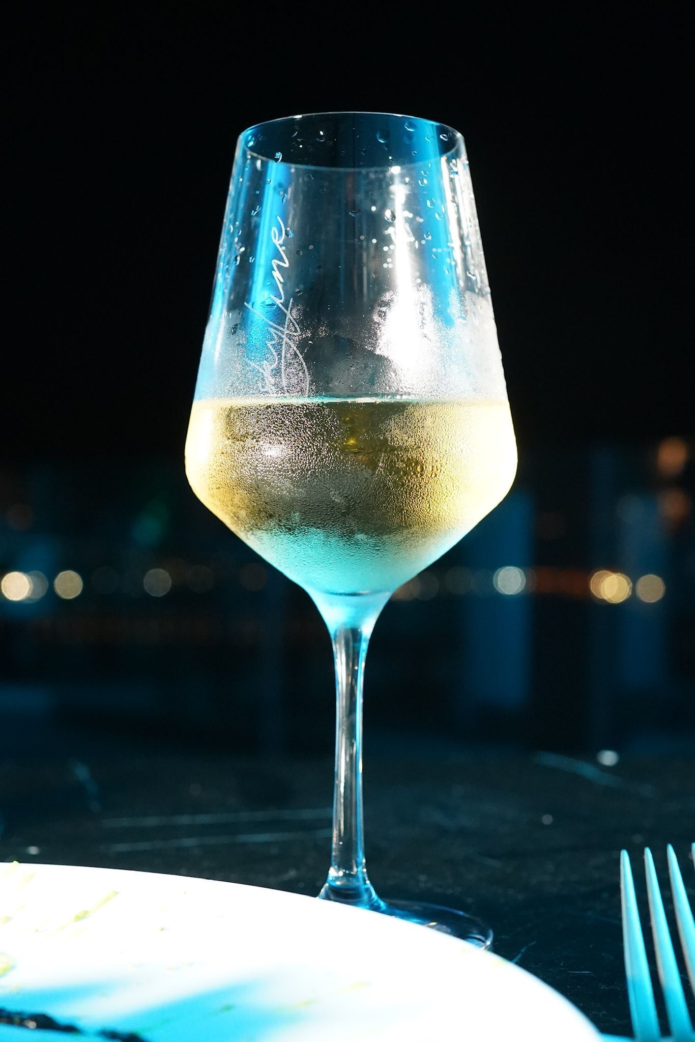 Bicchiere di champagne su un tavolo, bollicine che salgono. Sfondo blu e nero, ambiente elegante.