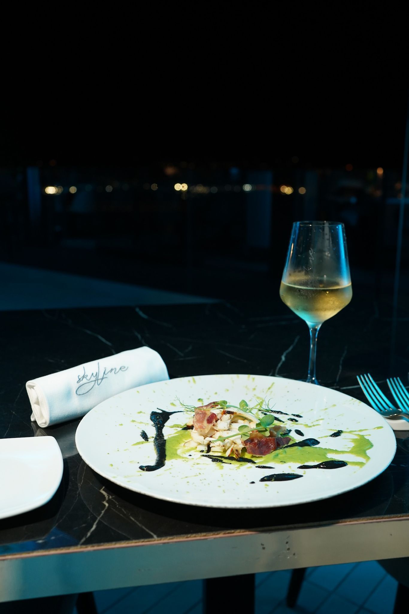 Un piatto di cibo, un bicchiere di vino e un tovagliolo arrotolato su un tavolo all'aperto di notte.