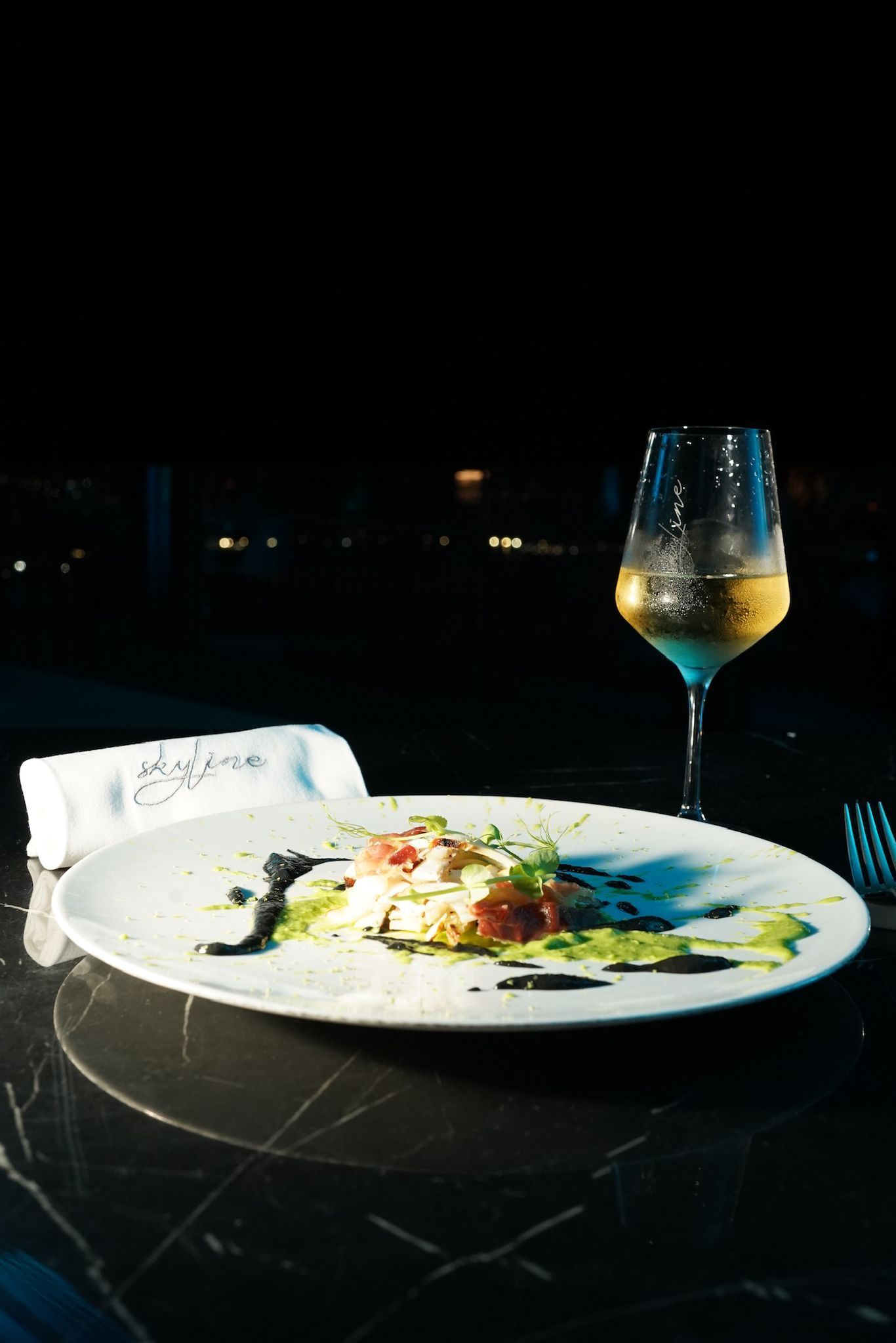 Un piatto di cibo con un bicchiere di vino bianco su un tavolo di marmo nero, scarsamente illuminato.