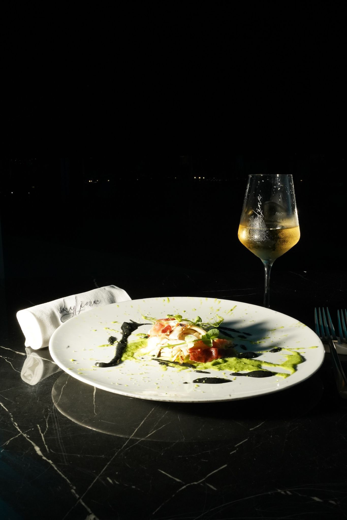 Un piatto di cibo con un bicchiere di vino bianco su un tavolo buio.