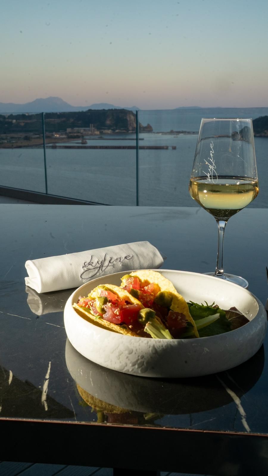 Tacos e vino su un tavolo con vista su uno specchio d'acqua al tramonto.