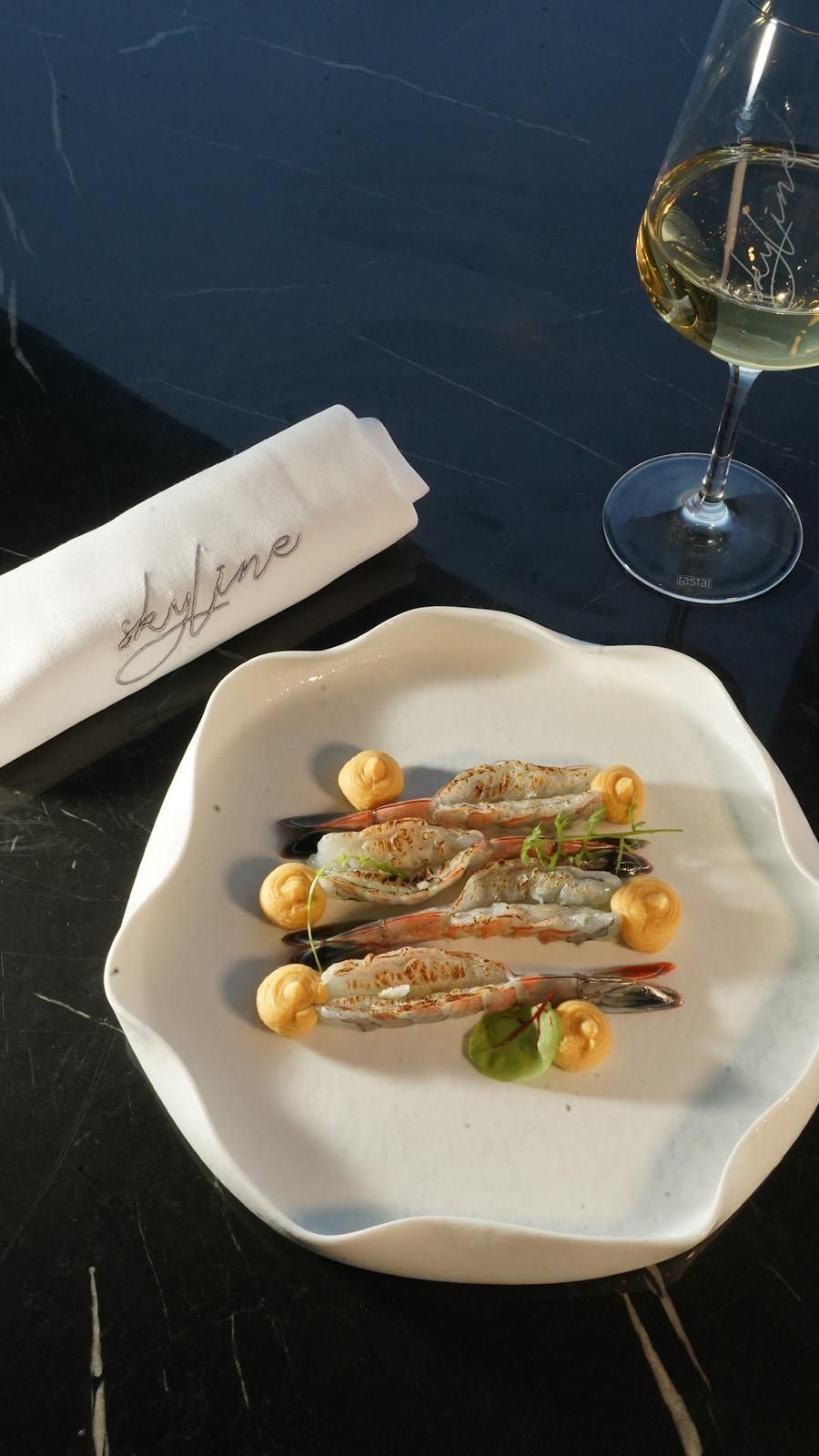 Piatto bianco con gamberi, contorno di vino e tovagliolo con scritta.