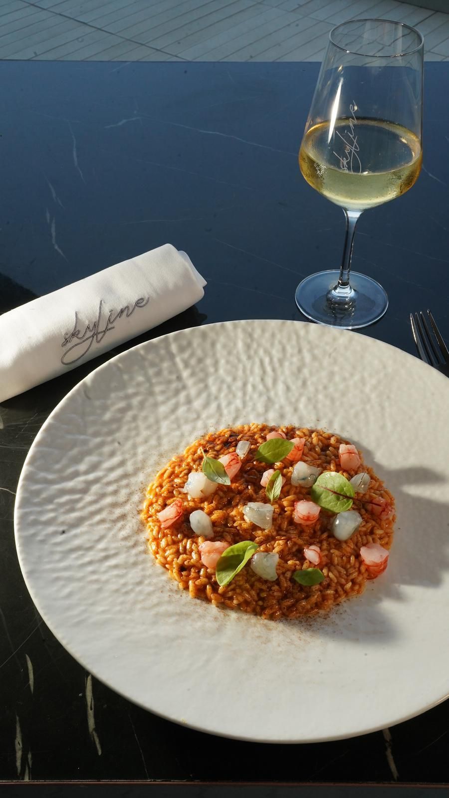 Piatto con contorno, bicchiere di vino e tovagliolo piegato su un tavolo.