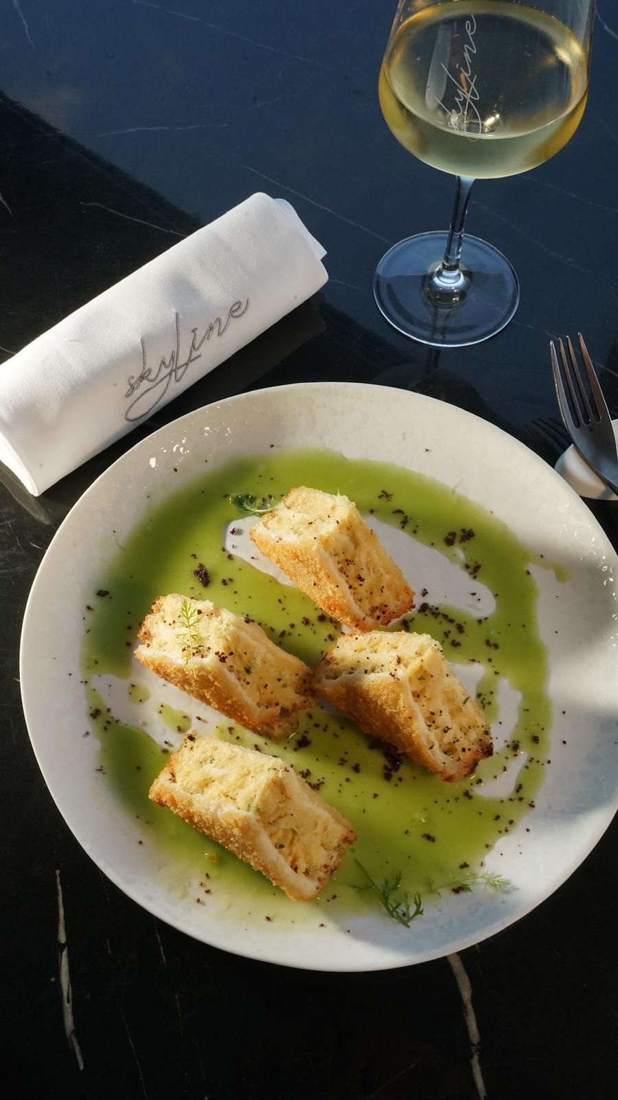Un piatto di pane con salsa verde, un bicchiere di vino, un tovagliolo e posate su un tavolo nero.