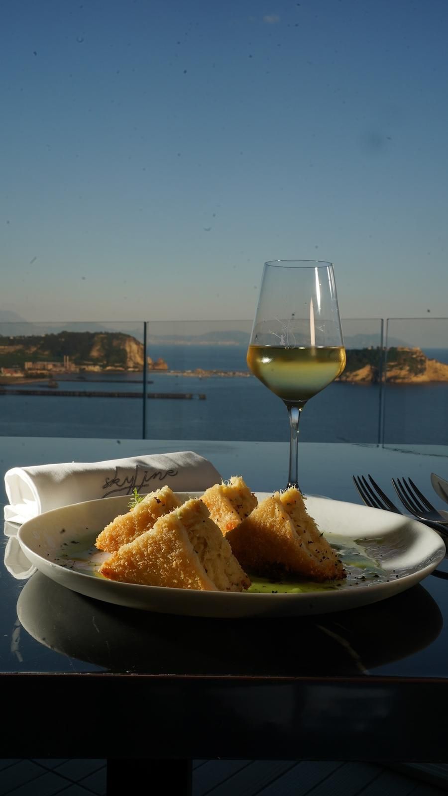 Un piatto di fritture e un bicchiere di vino bianco su un tavolo con vista sull'oceano.