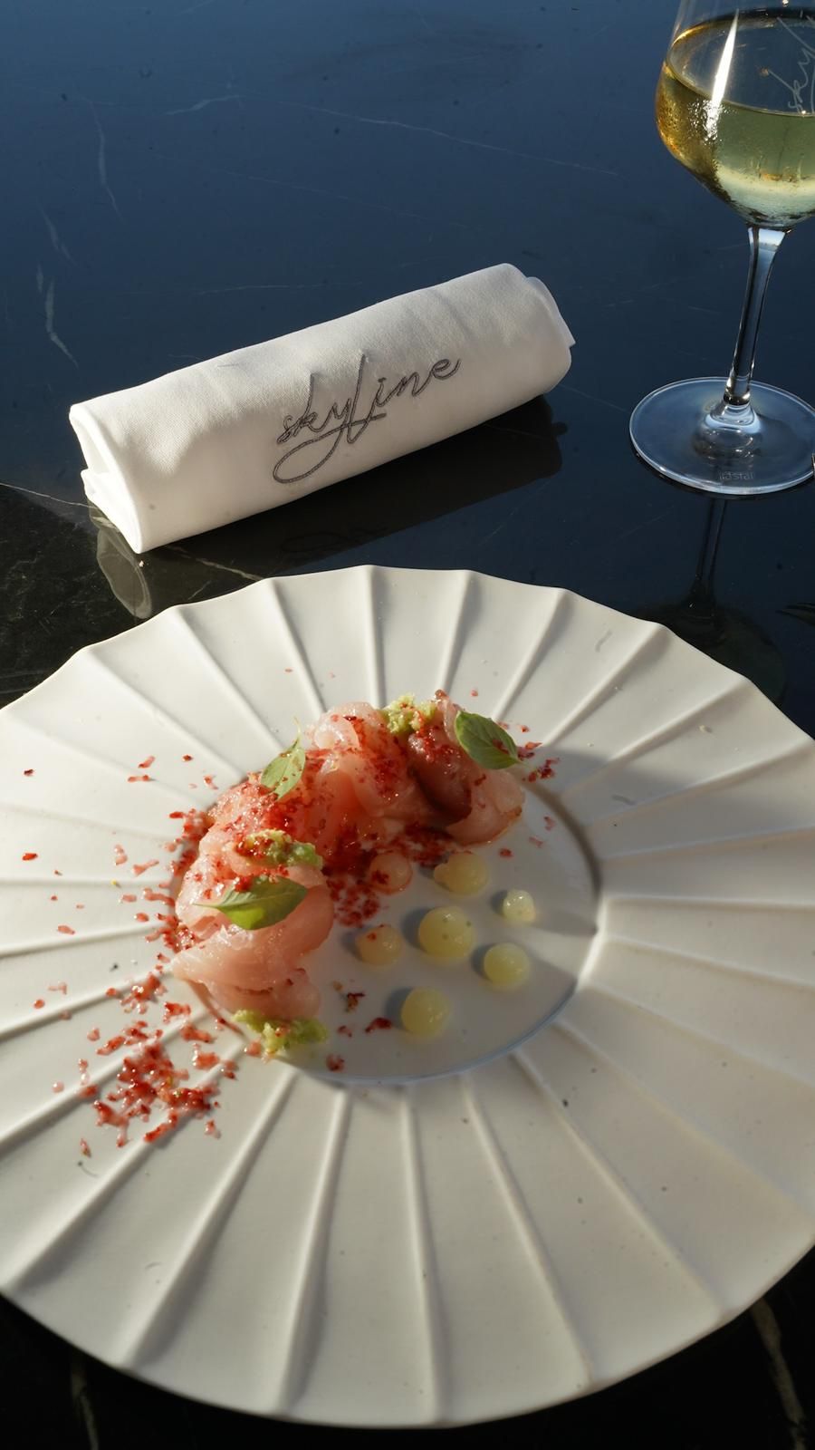 Piatto di cibo gourmet con vino bianco e un tovagliolo su una superficie nera.