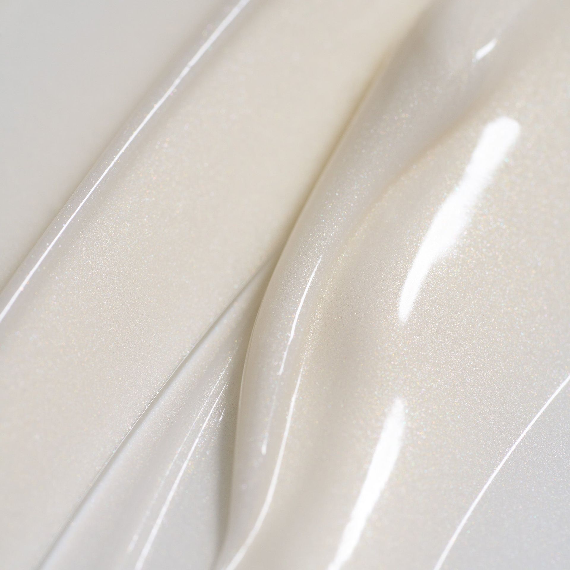 Two thick, swirling streaks of iridescent, pearlescent white cream or cosmetic gel on a clean surface.