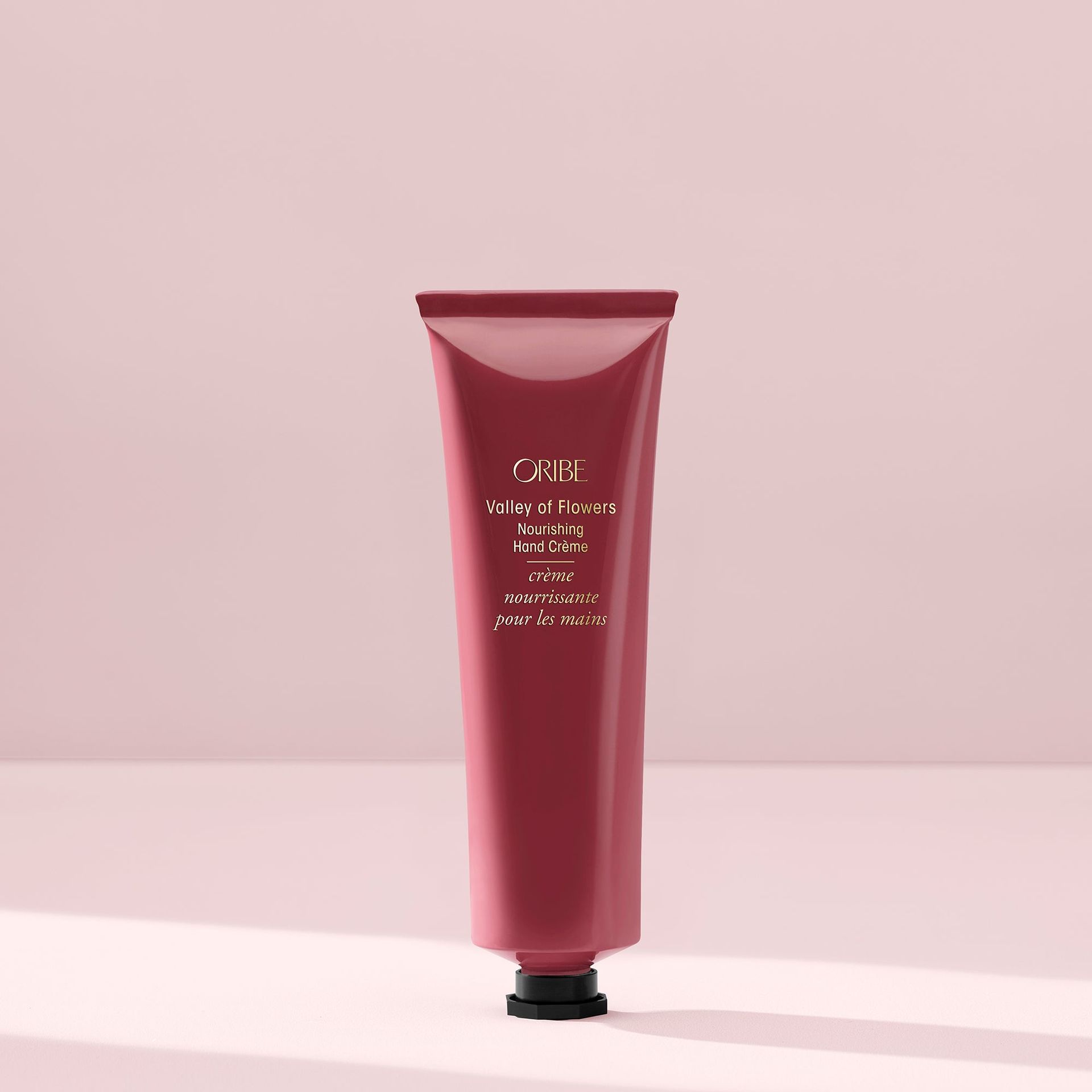 A mauve tube of Oribe Côte d’Azur restorative body crème standing upright against a light pink background.