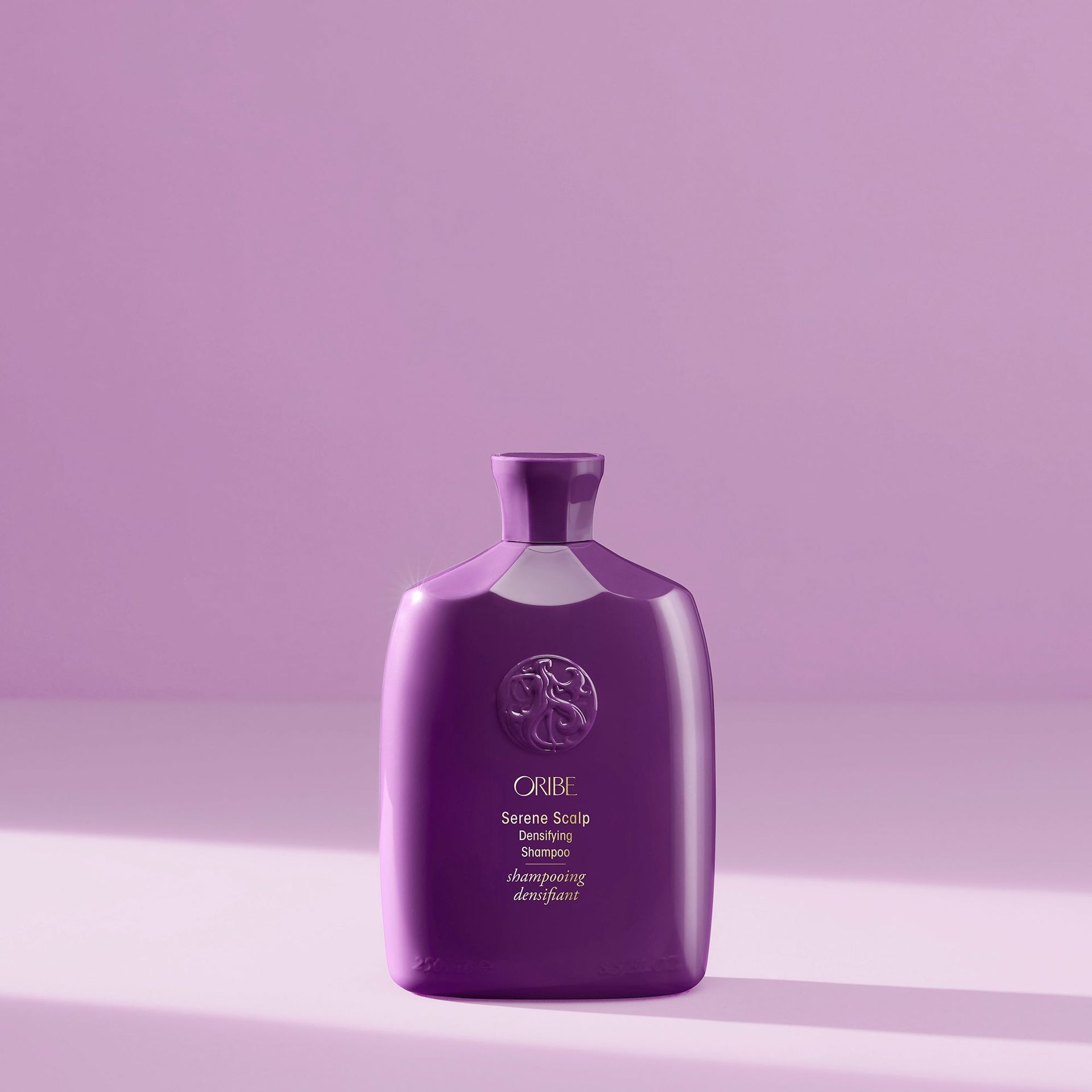 A purple bottle of Oribe Serene Scalp shampoo sits centered against a matching light purple background.
