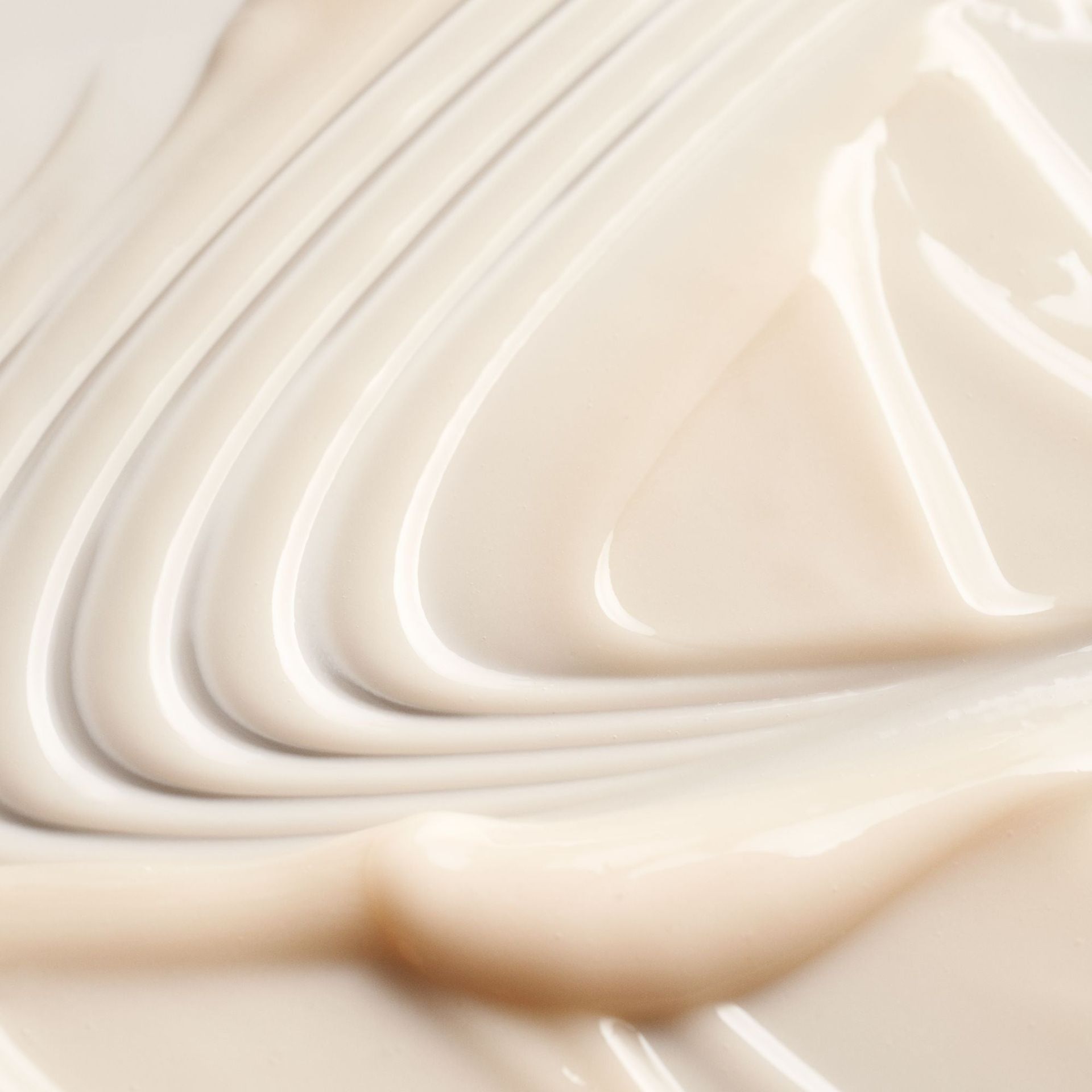 Creamy, off-white skincare product texture swirled into soft peaks and smooth, fluid lines.