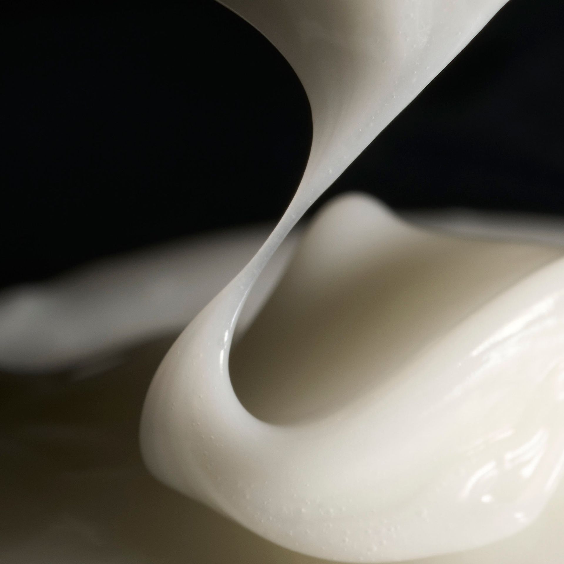 Thick, creamy white liquid flowing smoothly against a dark background, showing a glossy texture.