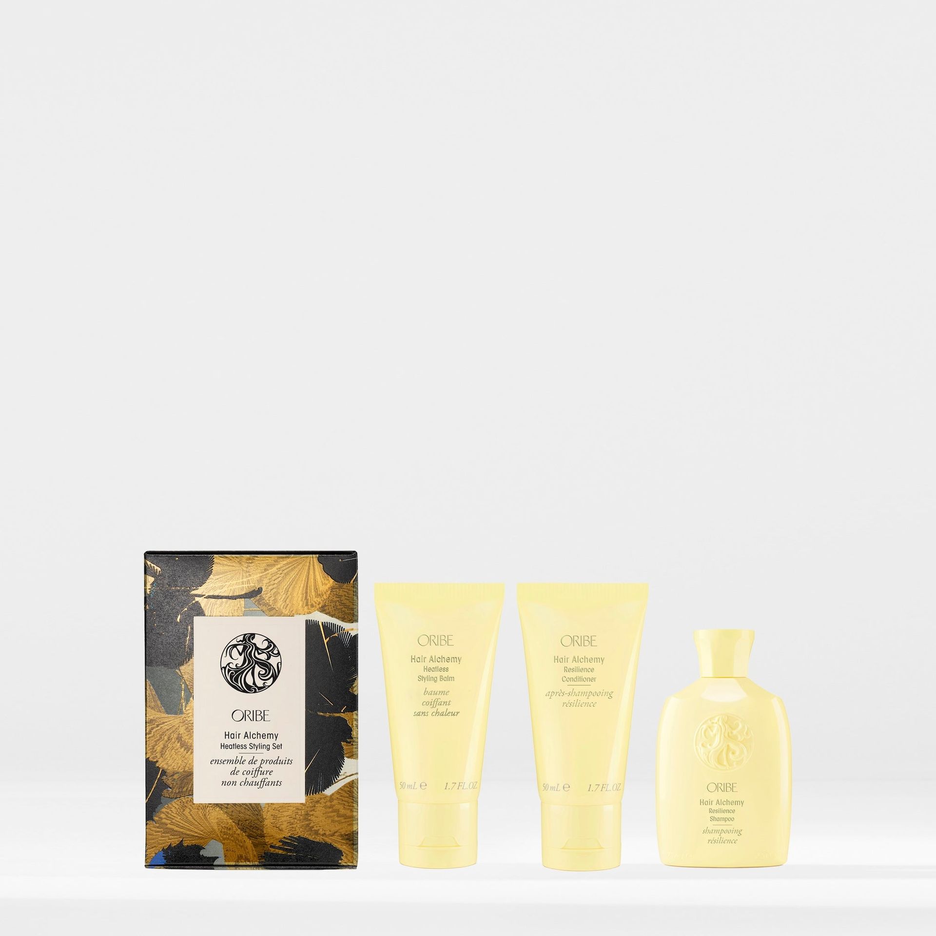 A product gift set featuring a patterned box, two yellow squeeze tubes, and a yellow bottle of Oribe haircare products.