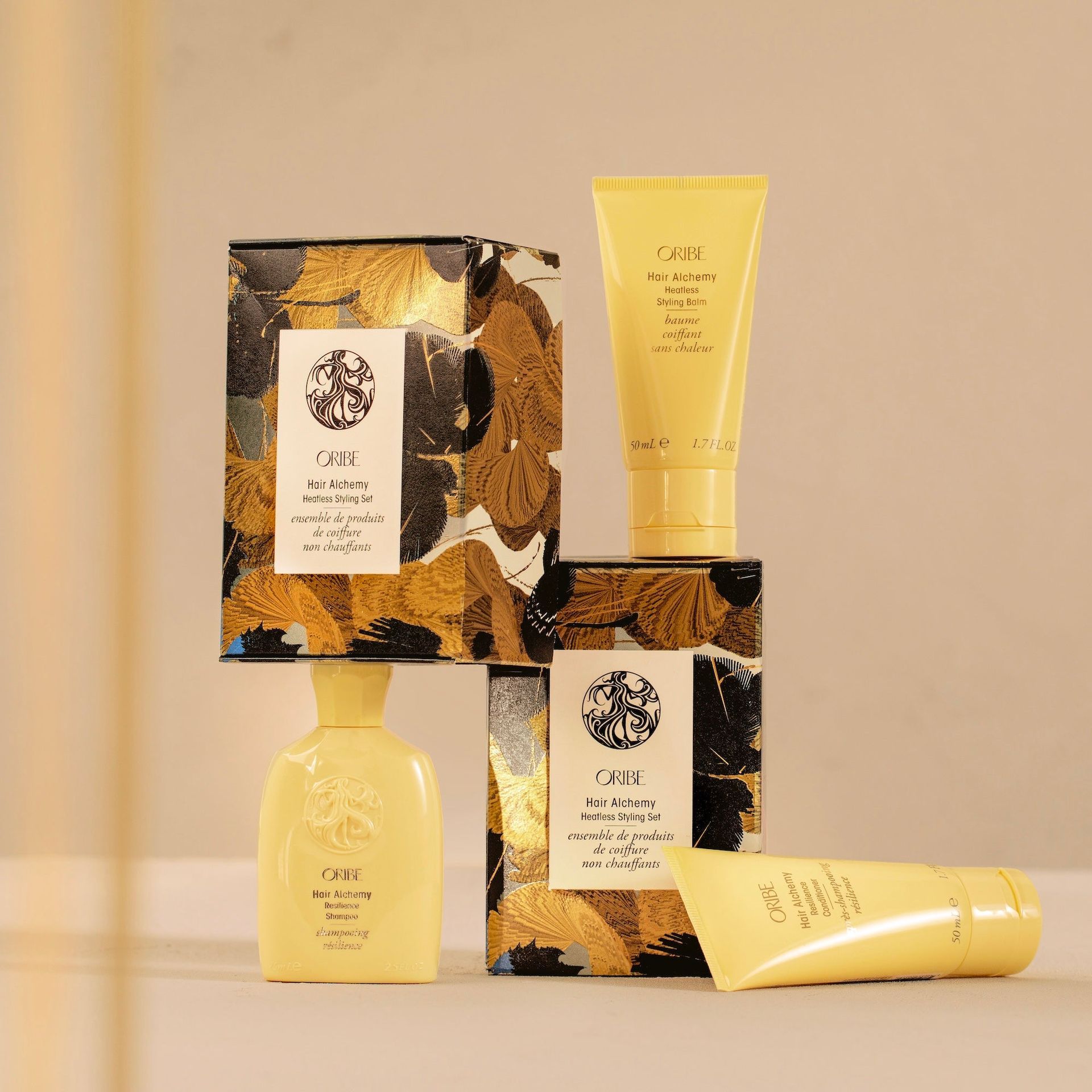 Three light yellow tubes and bottles of skincare products with decorative gold and black boxes against a beige background.