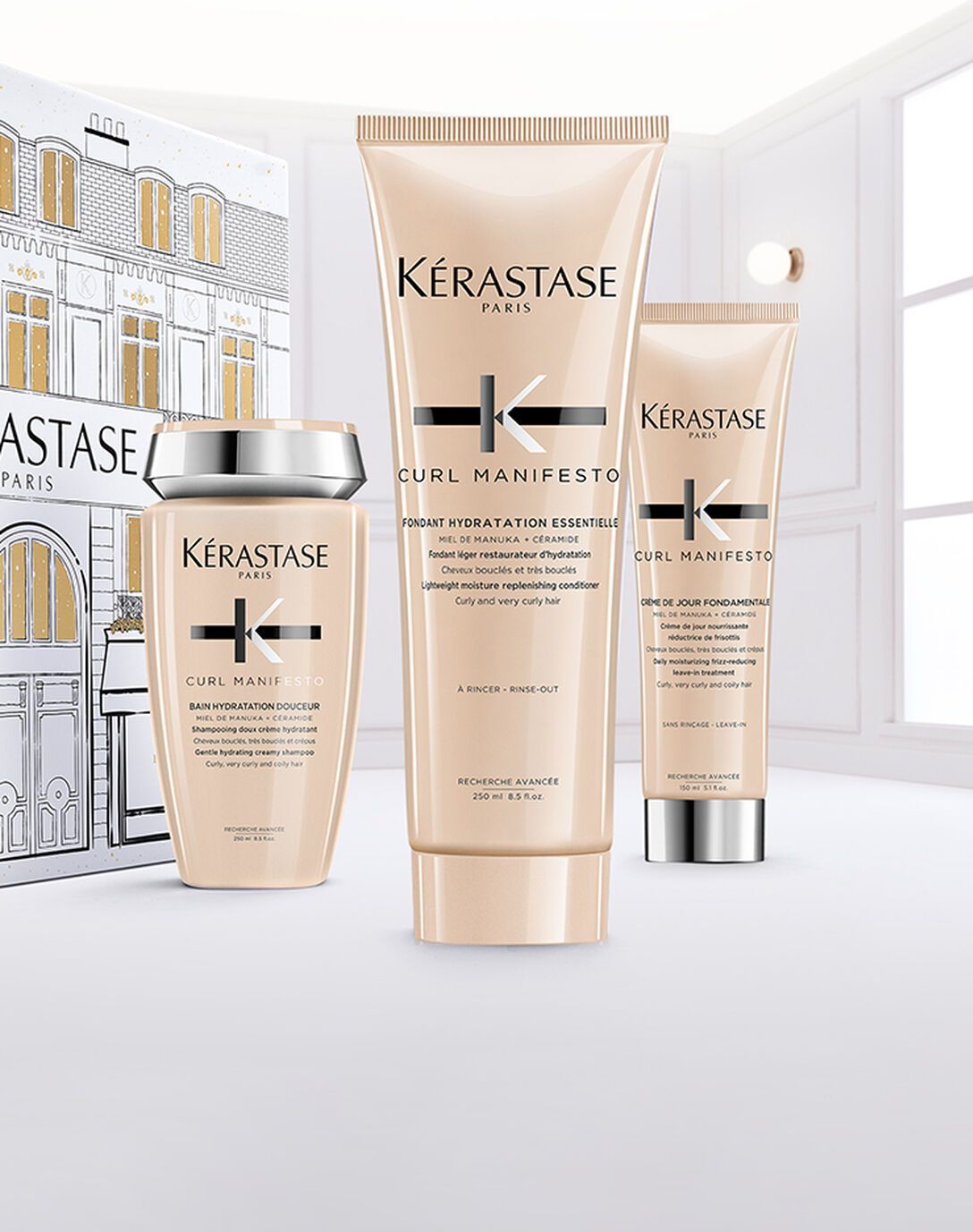 Three Kérastase hair care products arranged on a white surface with a branded gift box in the background.