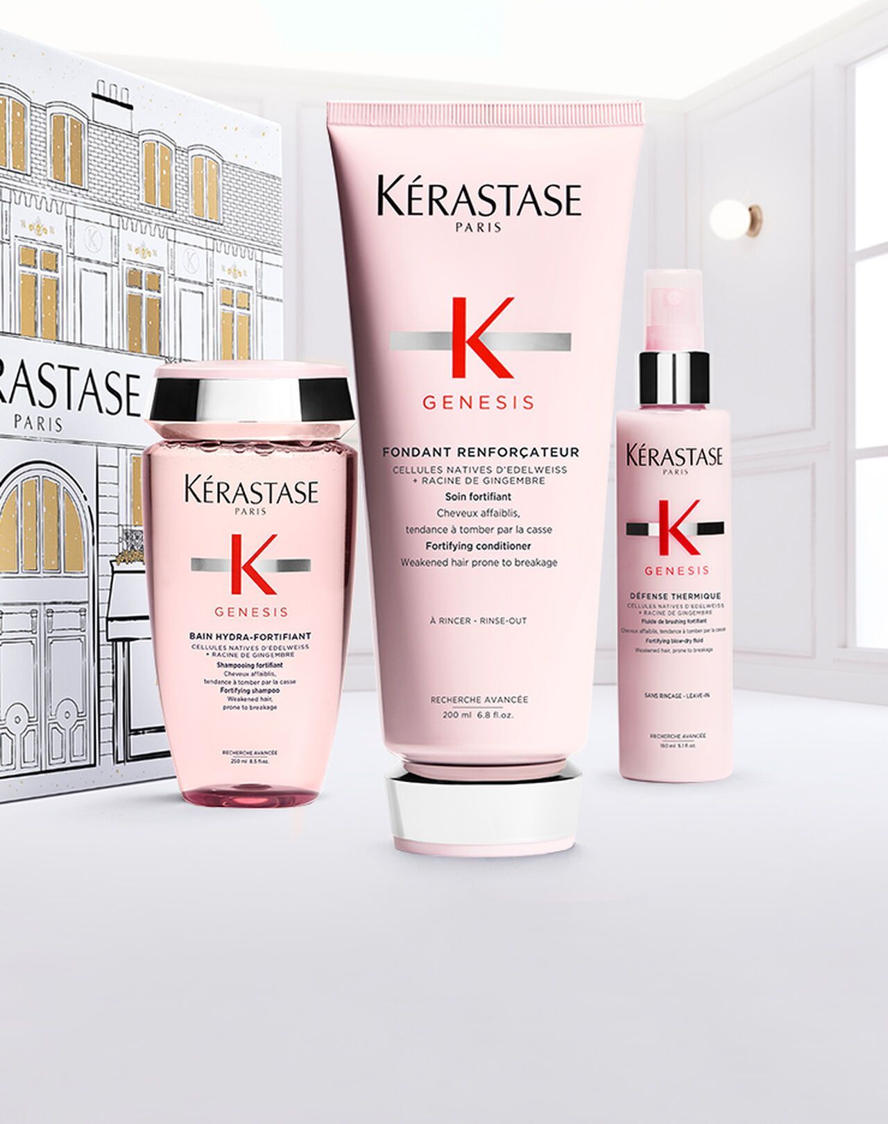 Three pink Kérastase Genesis hair care products arranged in front of a illustrated box against a bright, airy background.