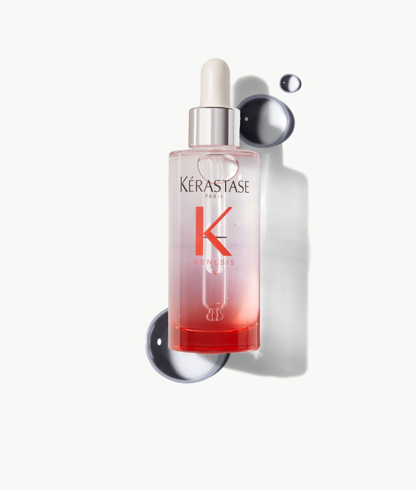 A bottle of Kérastase hair serum with a dropper, featuring a clear-to-red gradient, set against abstract grey shapes.