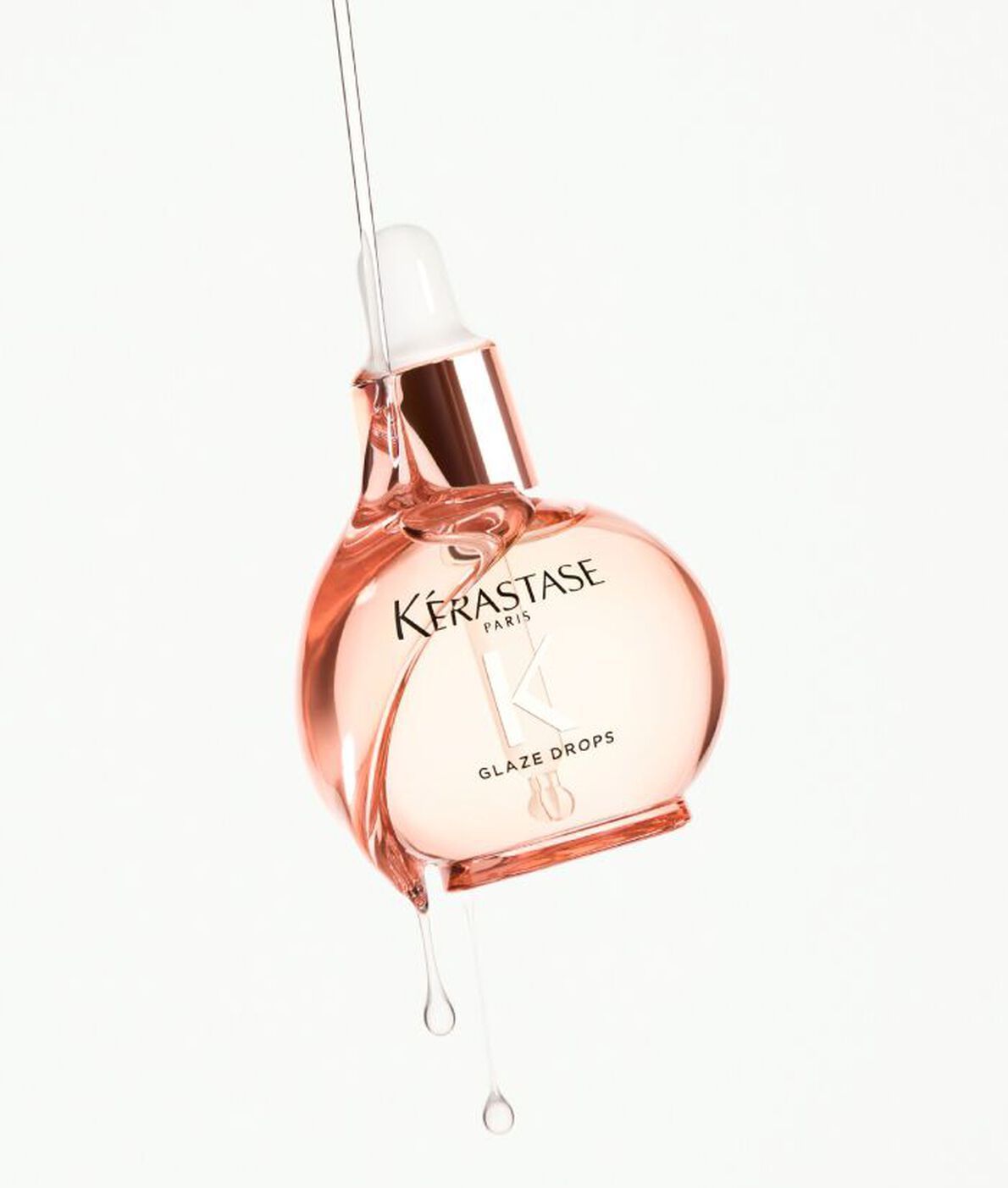 A Kérastase hair oil bottle suspended against a white background with product dripping from the applicator.