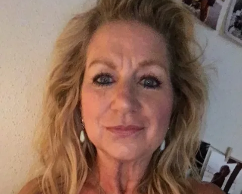 A person with long, blonde, wavy hair facing the camera with a neutral expression.