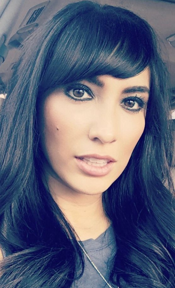 A headshot of a person with long, dark, wavy hair and bangs, looking directly at the camera with a neutral expression.