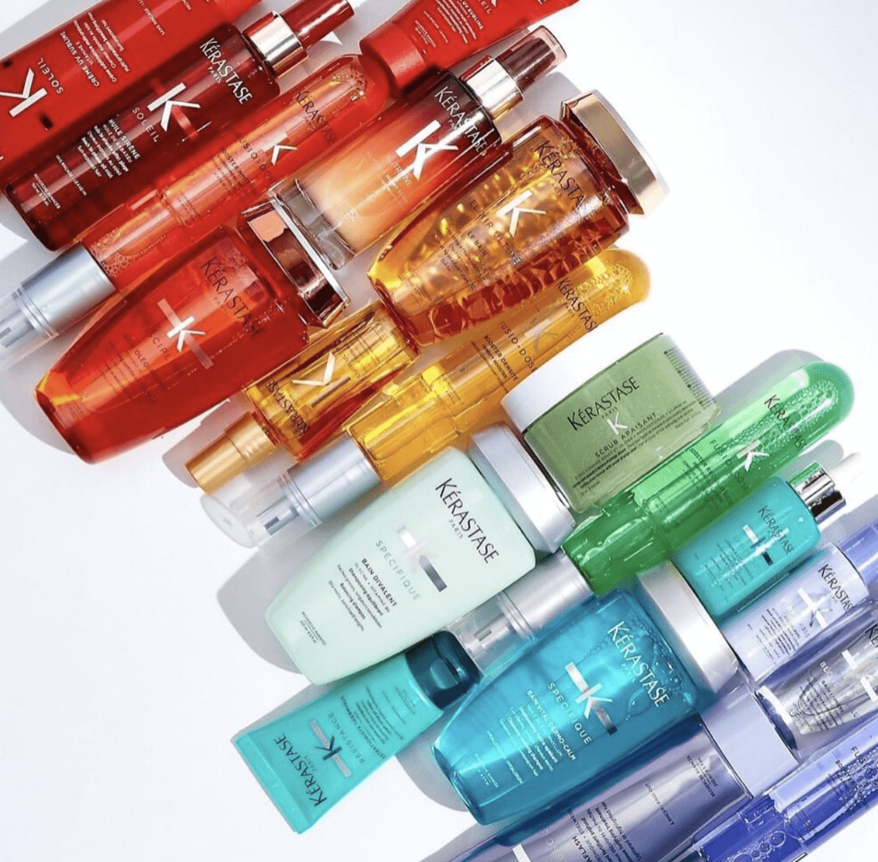 A collection of Kérastase hair care bottles and jars arranged in a diagonal rainbow color gradient on a white background.