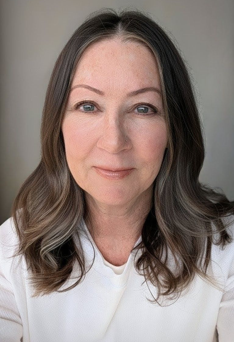 A portrait of a person with shoulder-length, wavy dark hair and a neutral expression, wearing a white shirt.