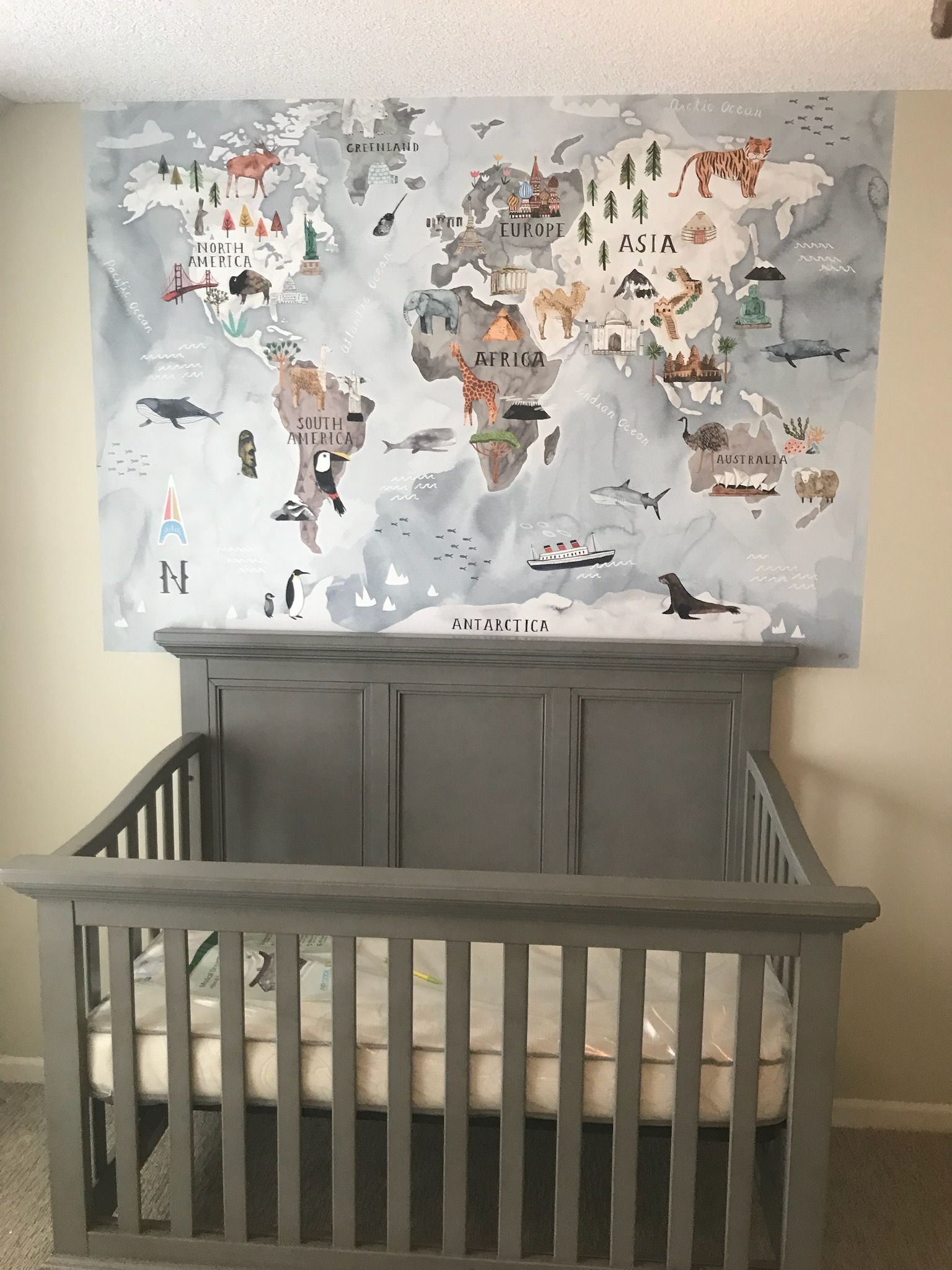 A crib in a nursery with a map of the world on the wall behind it.