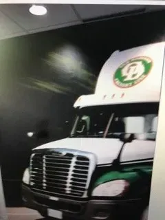 A white and green semi truck is parked in front of a black wall.