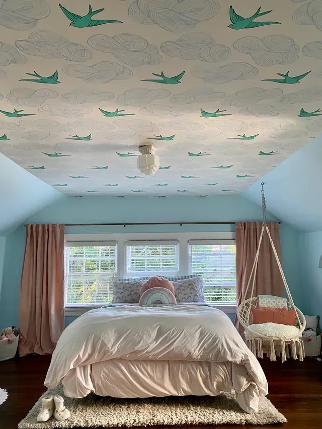 A bedroom with a bed , chair , and ceiling with birds on it.