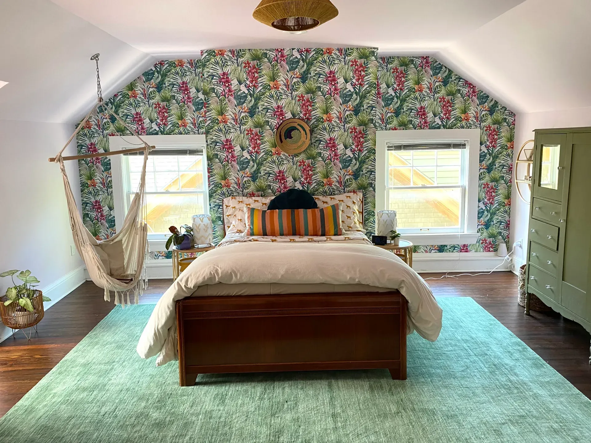 A bedroom with a bed , hammock , dresser and floral wallpaper.