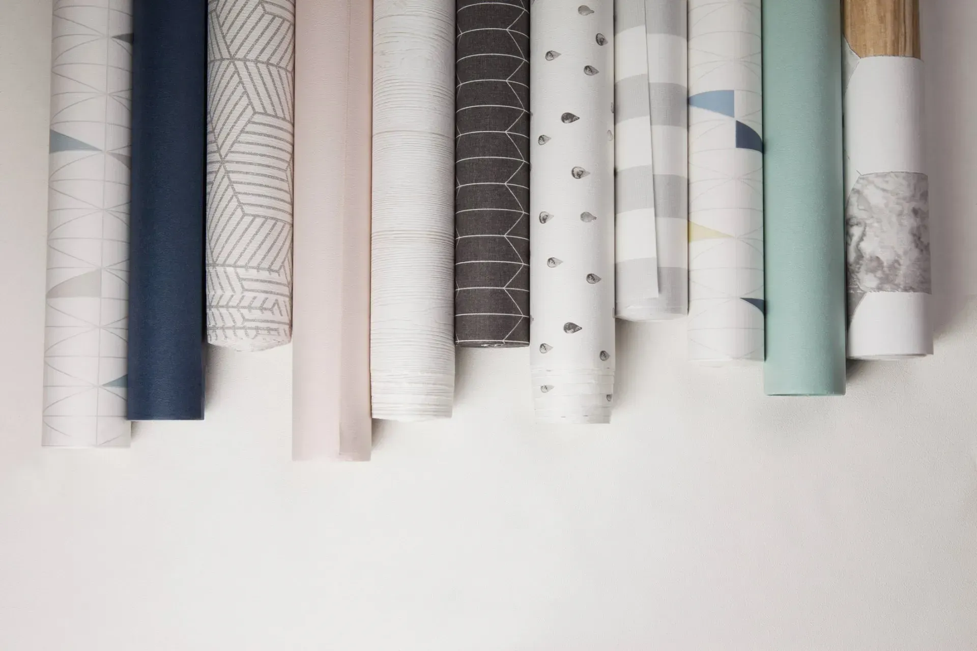 A row of rolls of wallpaper hanging on a white wall.