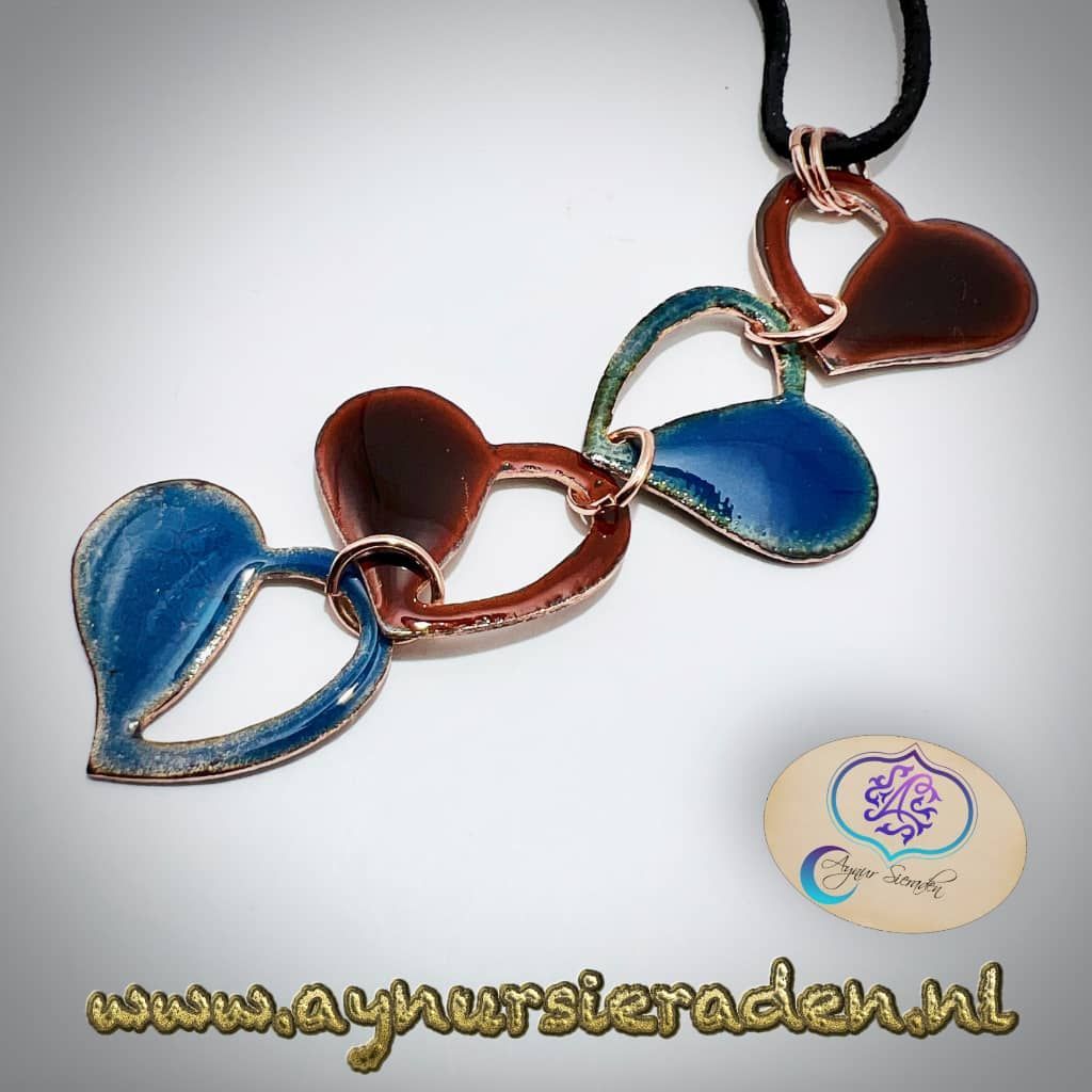 Deze hanger is versierd met vier geëmailleerde hartjes. De basis van de hanger is van koper. De bijbehorende leren ketting heeft een koperen haakslot.