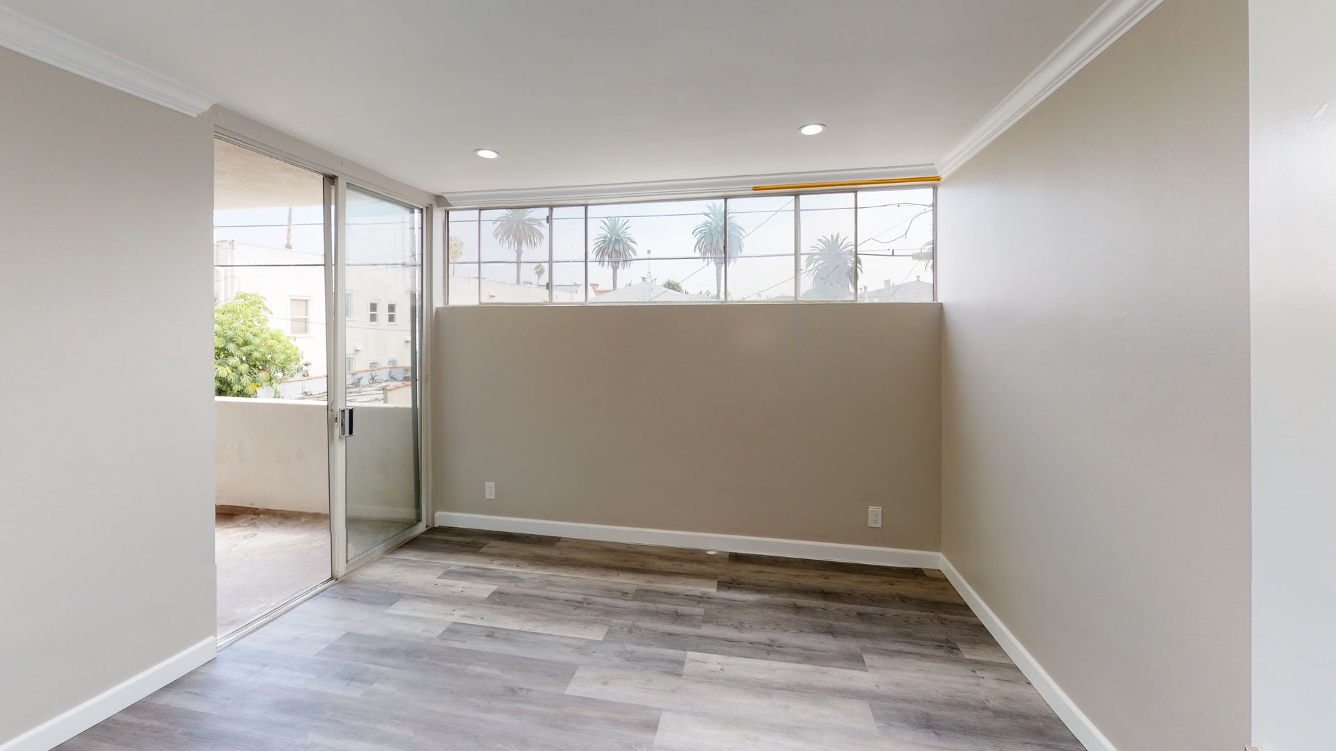 Empty room with sliding glass door to balcony, and windows above a wall. Grey flooring and beige walls.
