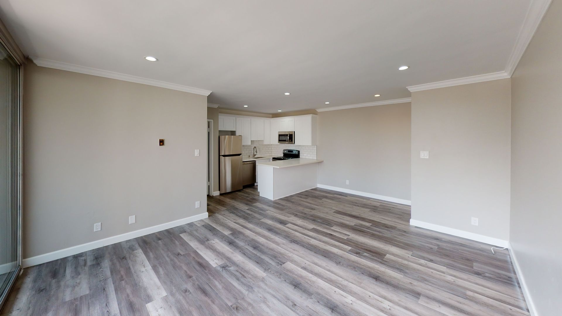 Empty apartment interior with kitchen in the background. Light wood-look flooring, beige walls, and white cabinets.