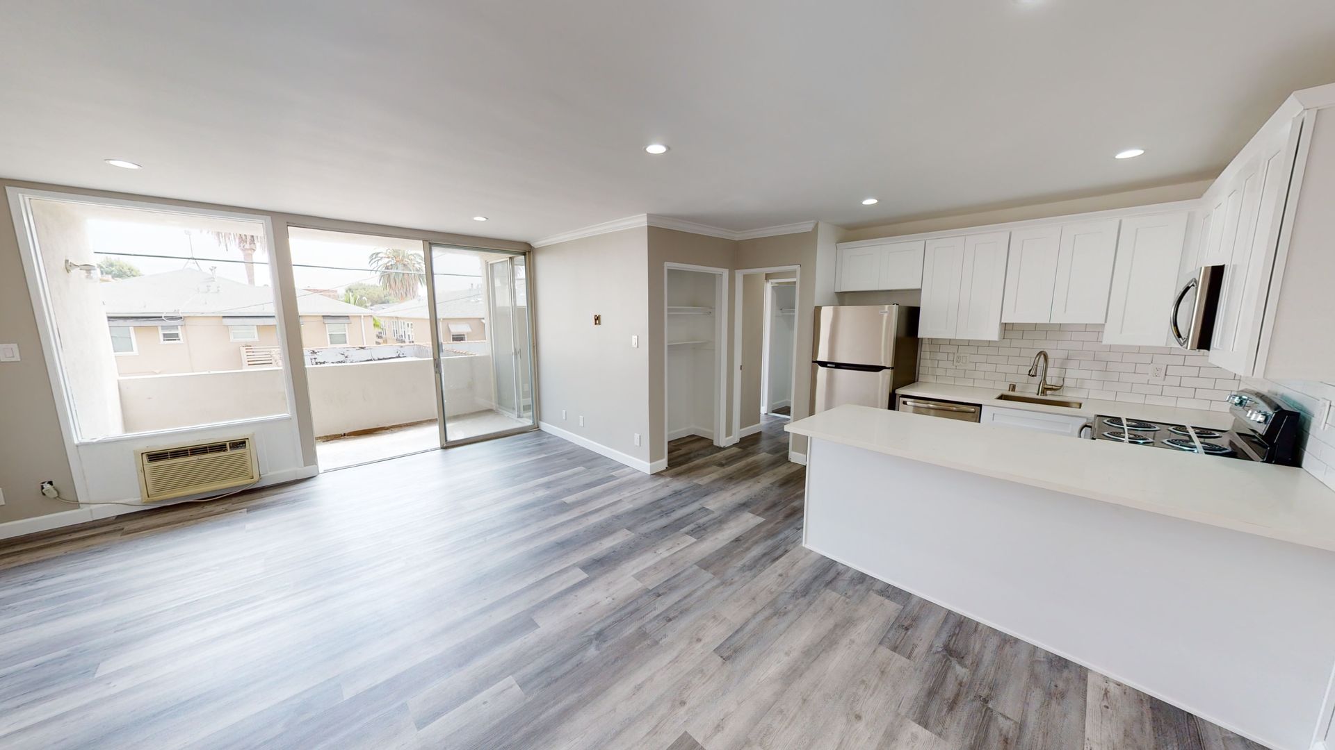 Interior view of a modern apartment with kitchen, living area, balcony, and gray wood-look flooring.