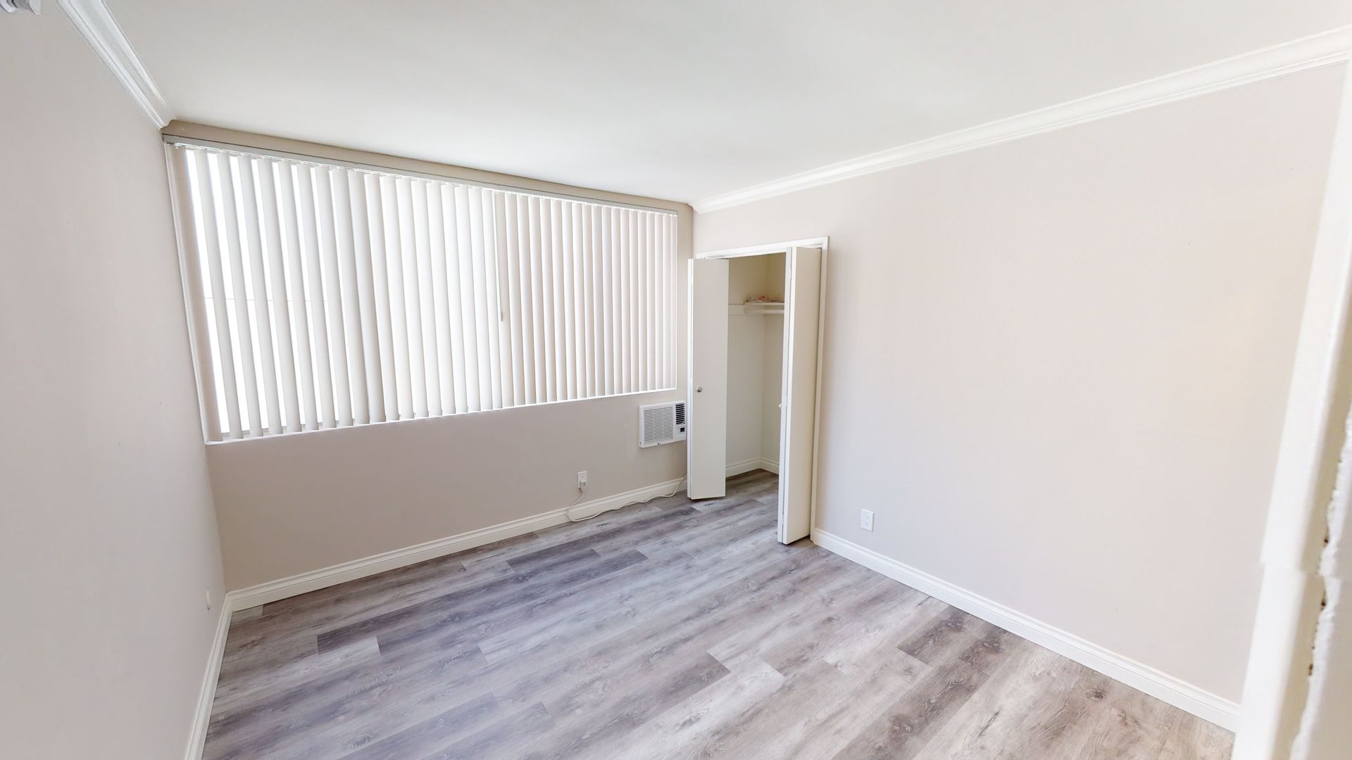Empty bedroom with gray wood-look flooring, a closet, and a window with blinds.