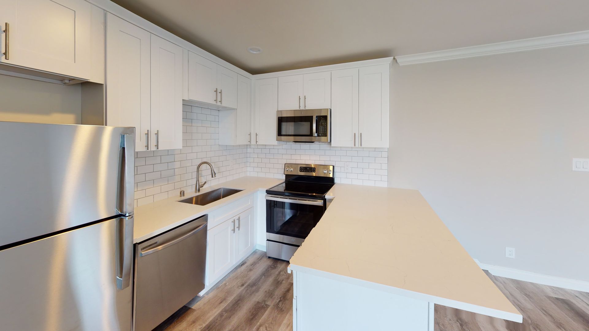 Modern kitchen with white cabinets, stainless steel appliances, and a white countertop island.