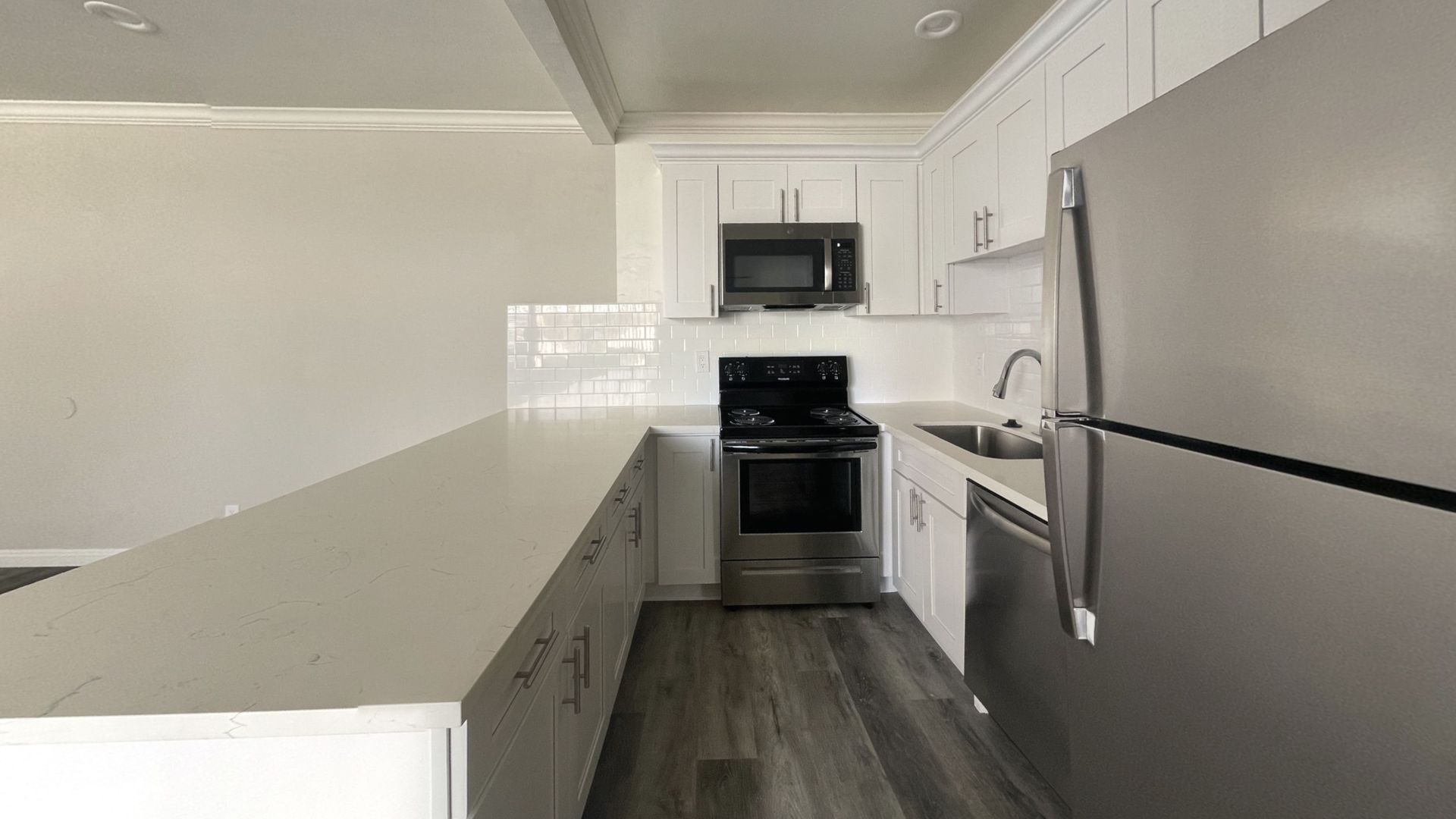 Modern kitchen with white cabinets, stainless steel appliances, and a long countertop.