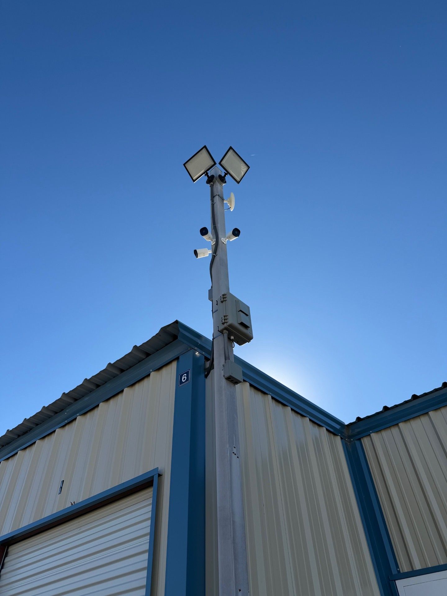 Security pole with cameras and lights mounted on a building corner against a blue sky.